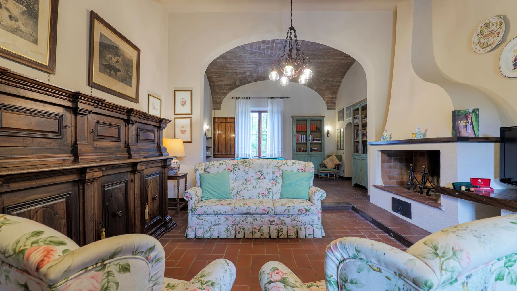 A living room with floral seating, dark wood paneling, and an arched ceiling.