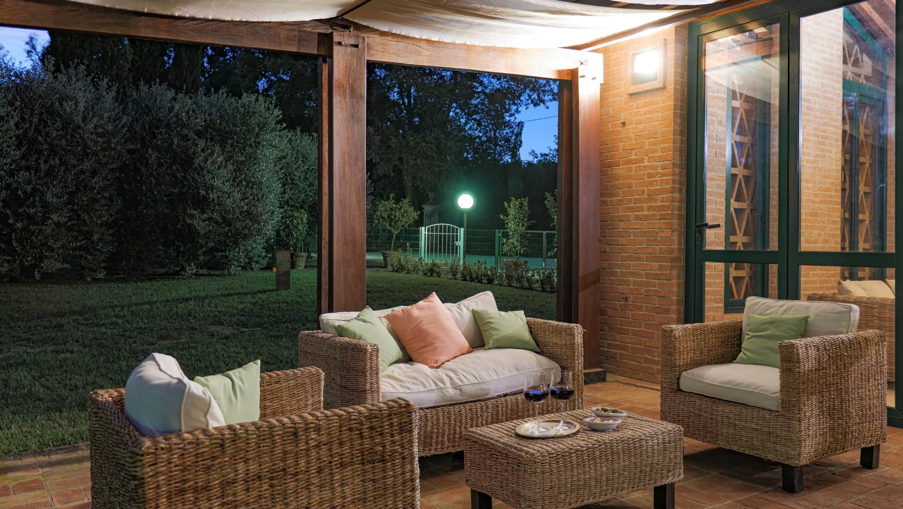 An outdoor seating area with wicker furniture and cushions beside a garden.