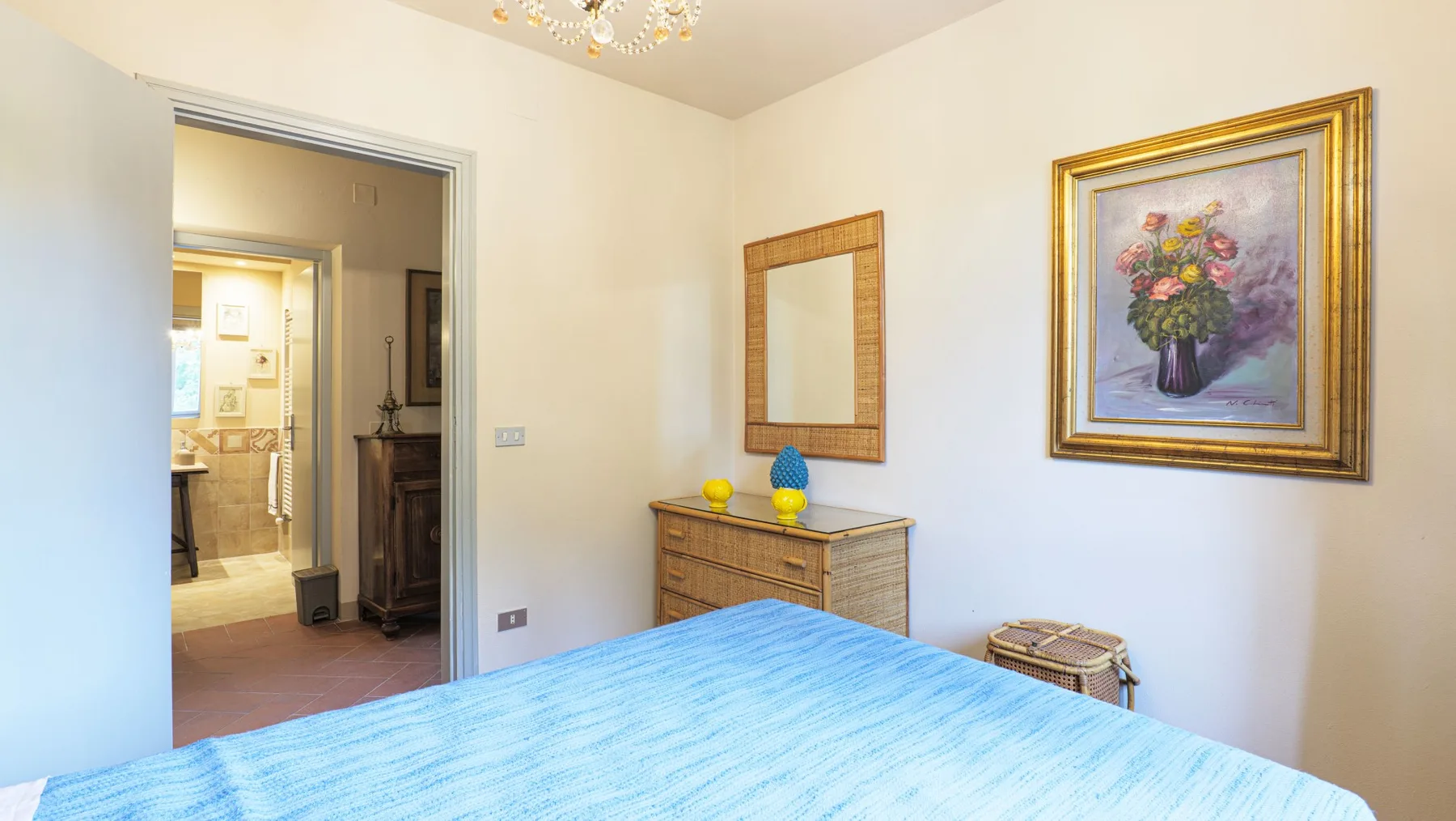 A bedroom with blue bedding, a dresser, and framed wall art.