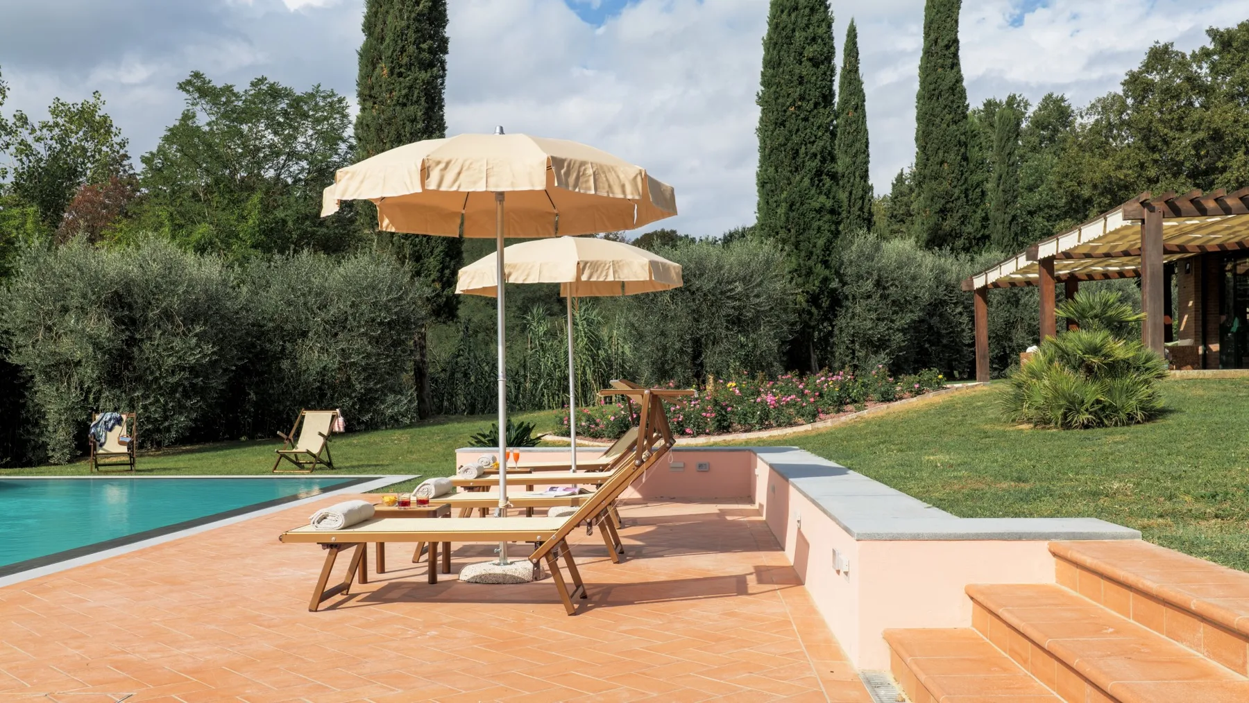 A poolside terrace has sun loungers, umbrellas, and steps beside the water.