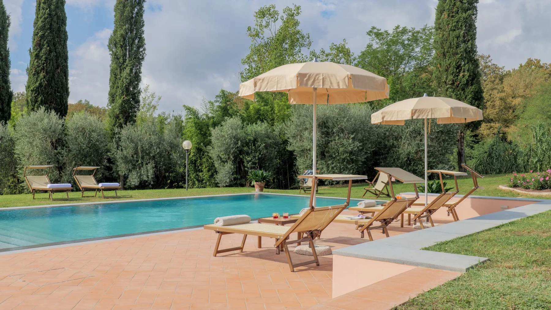 An outdoor swimming pool with lounge seating and umbrellas beside a garden.
