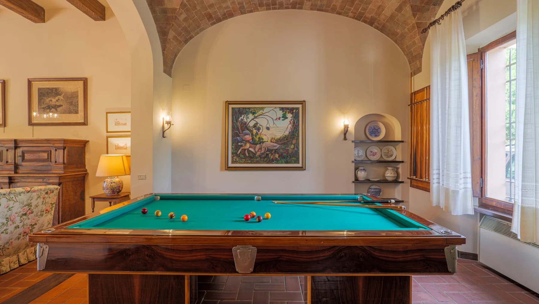 A billiards room with a green-felt table beneath a brick ceiling.