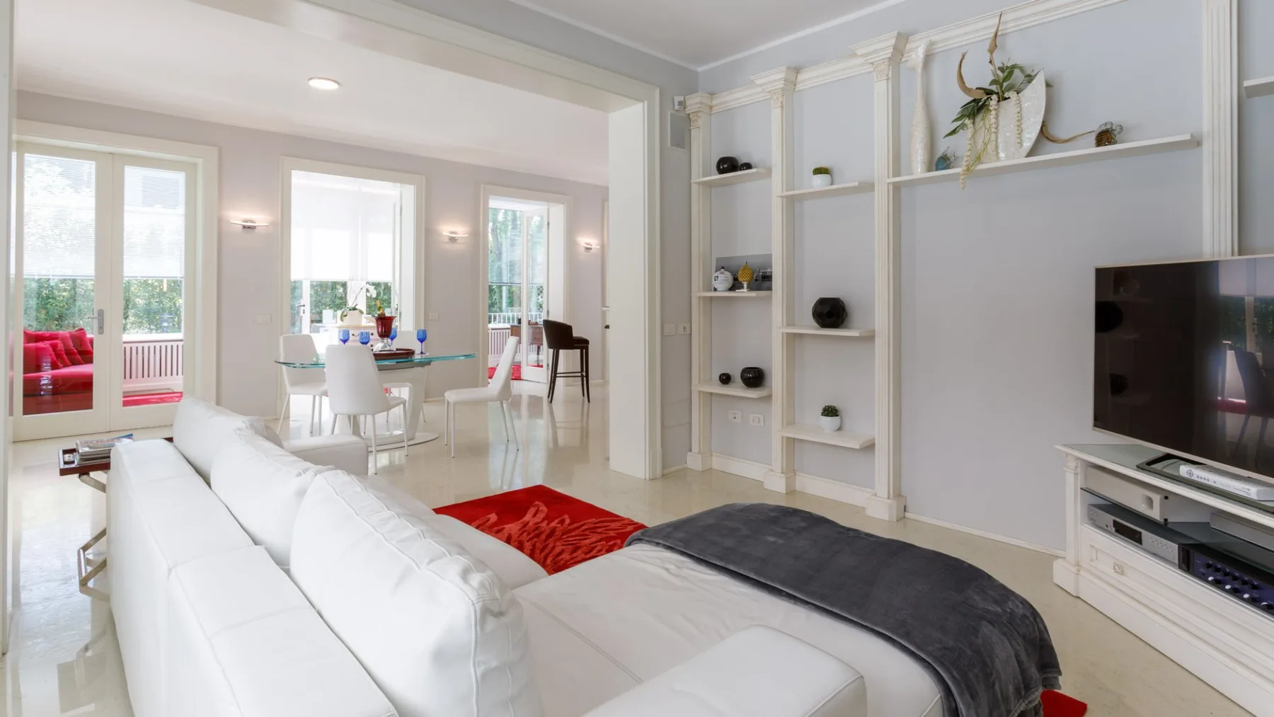 Una luminosa sala de estar y comedor con asientos blancos, una mesa y estanterías empotradas.