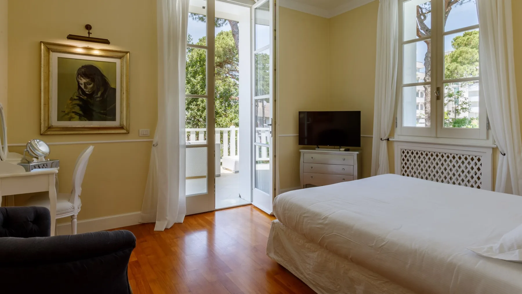Un dormitorio con una cama, un televisor y ventanas altas que dan a un balcón.