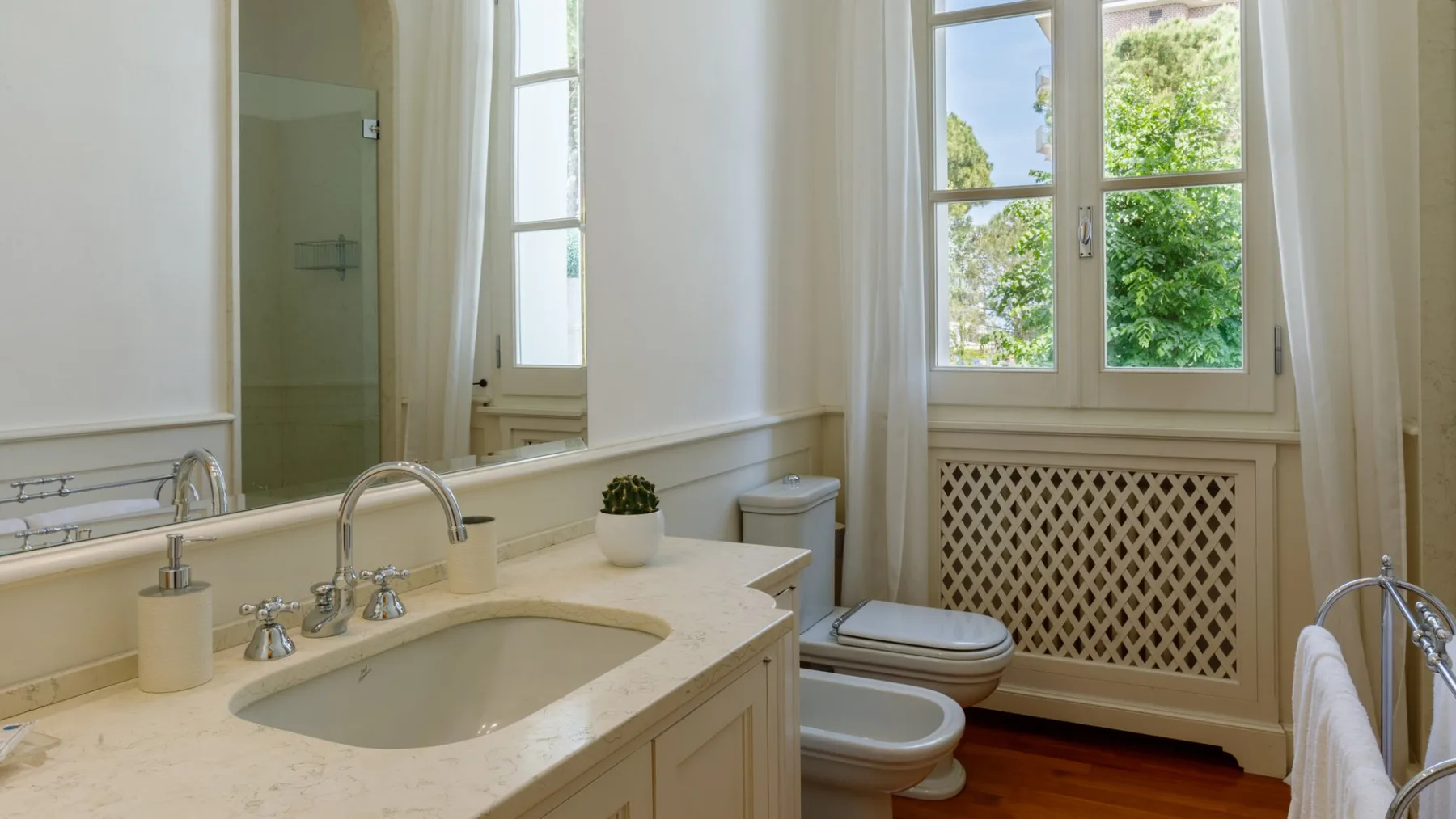 Un baño luminoso con lavabo, inodoro y una ventana con vistas a la vegetación.