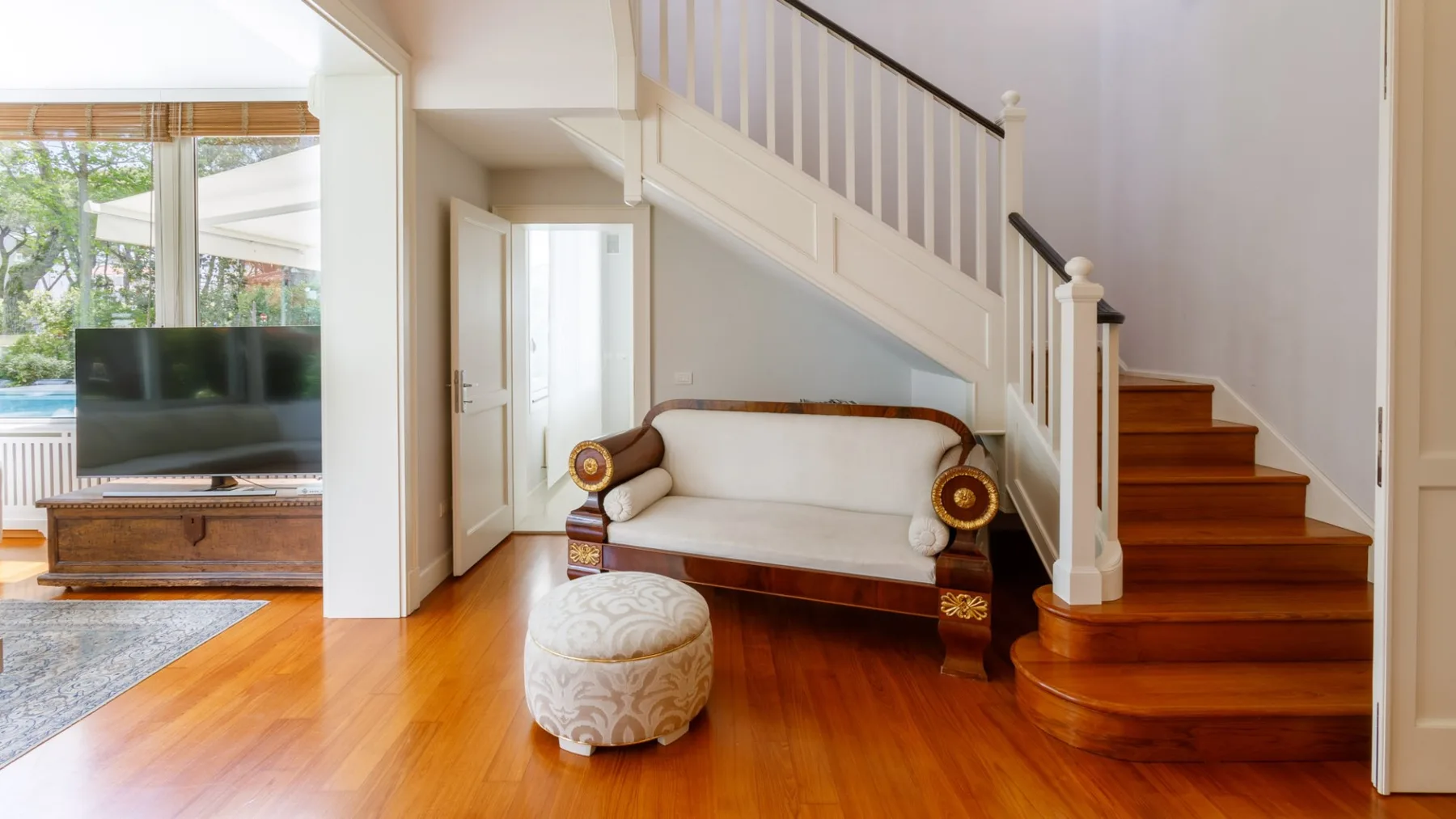 Una sala de estar con un sofá crema bajo una escalera de madera.