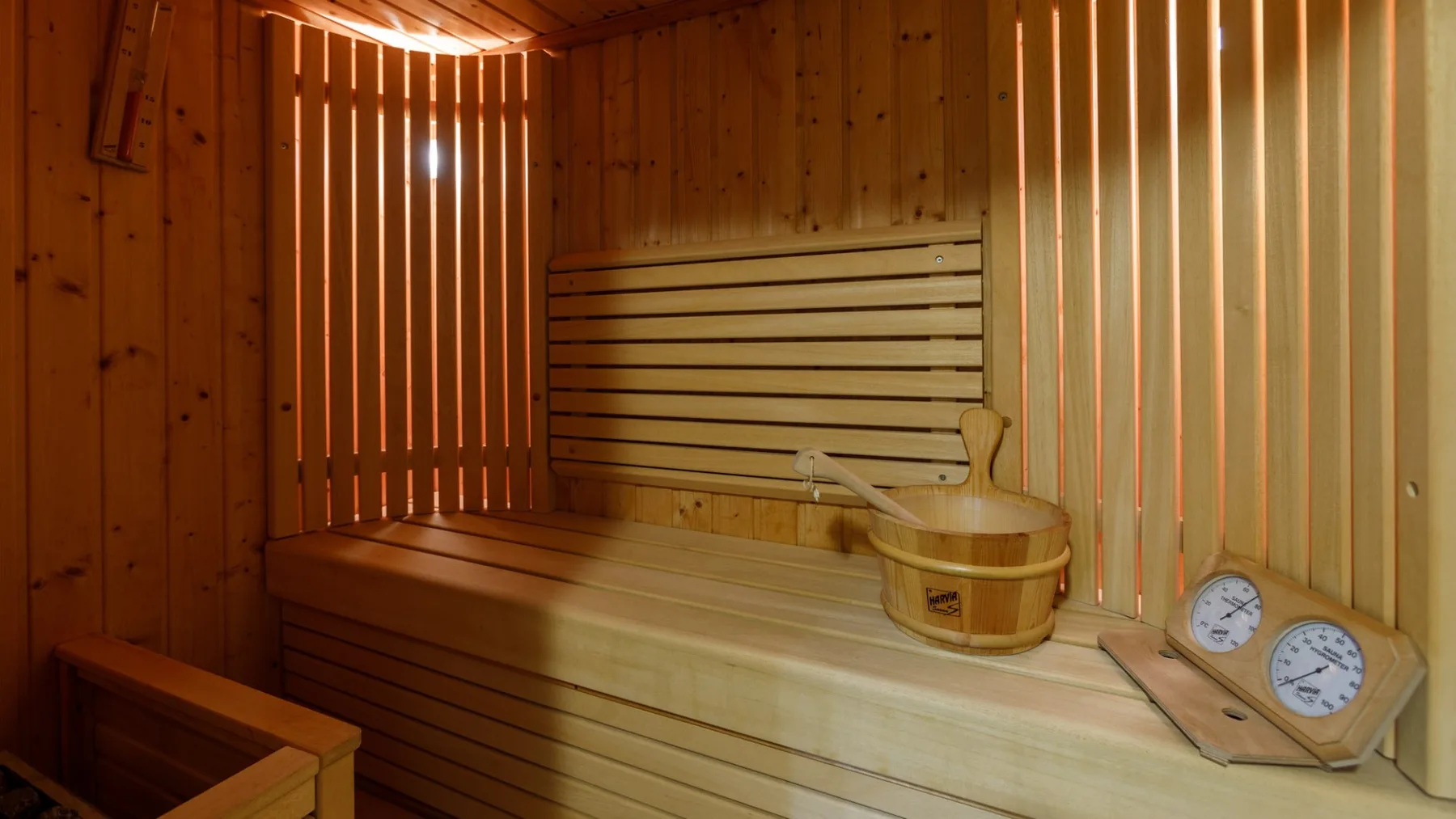 Interior de sauna de madera con un banco, un cubo y un termómetro en la pared.