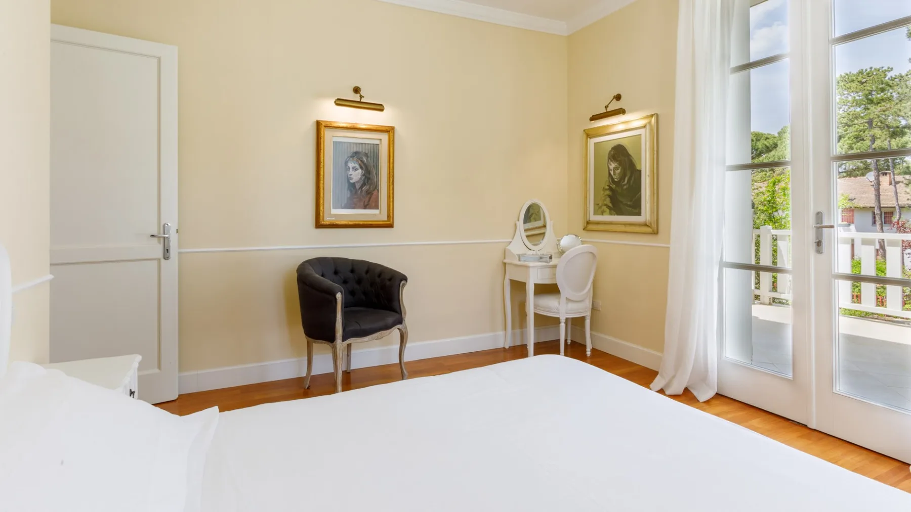 Un dormitorio con una cama, un pequeño escritorio y ventanales altos.