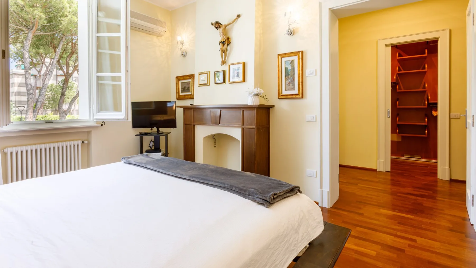 Un dormitorio con una cama grande, una chimenea y una puerta abierta a un pasillo con suelo de madera.