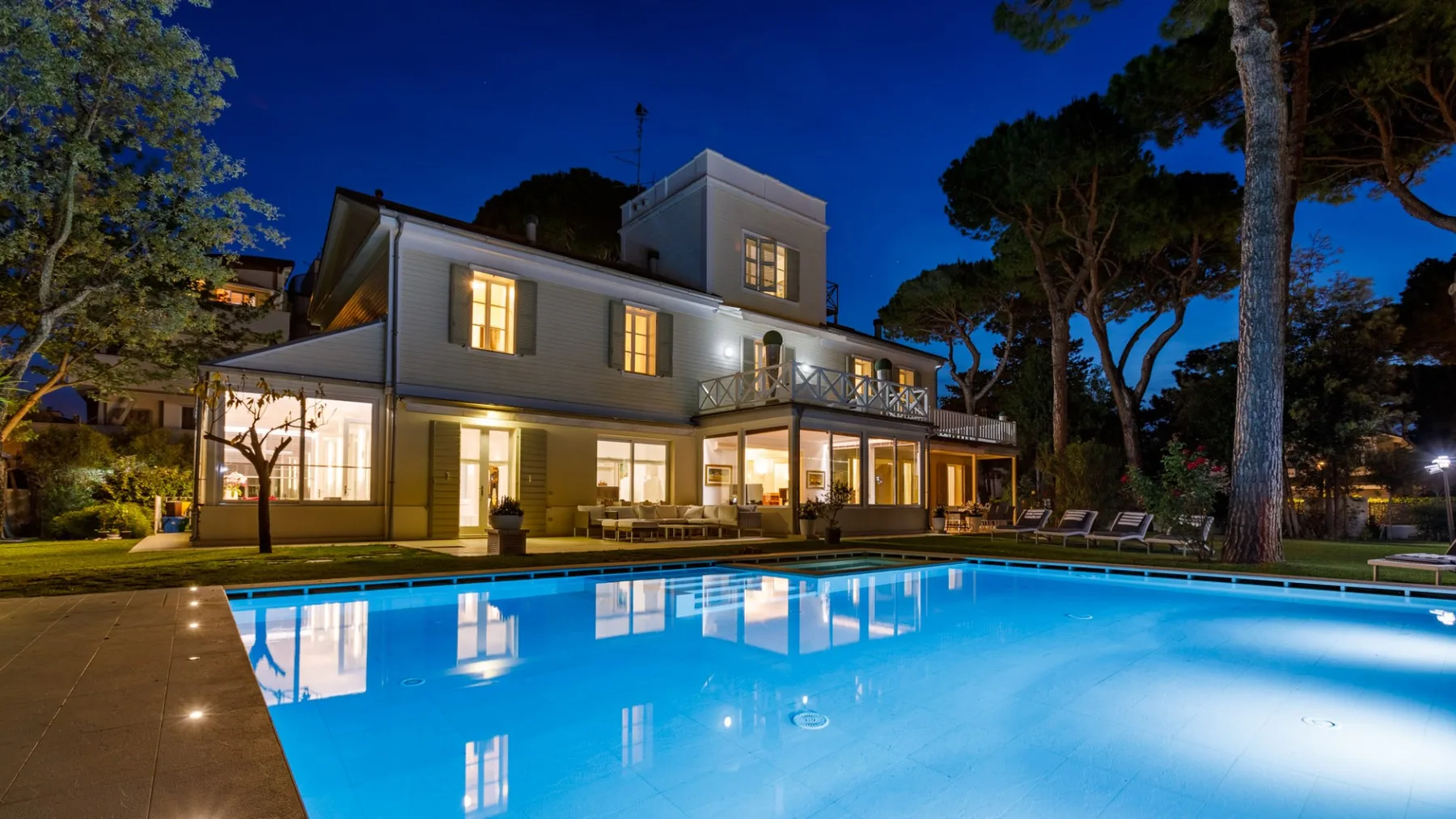 Una casa iluminada está junto a una piscina resplandeciente al anochecer.