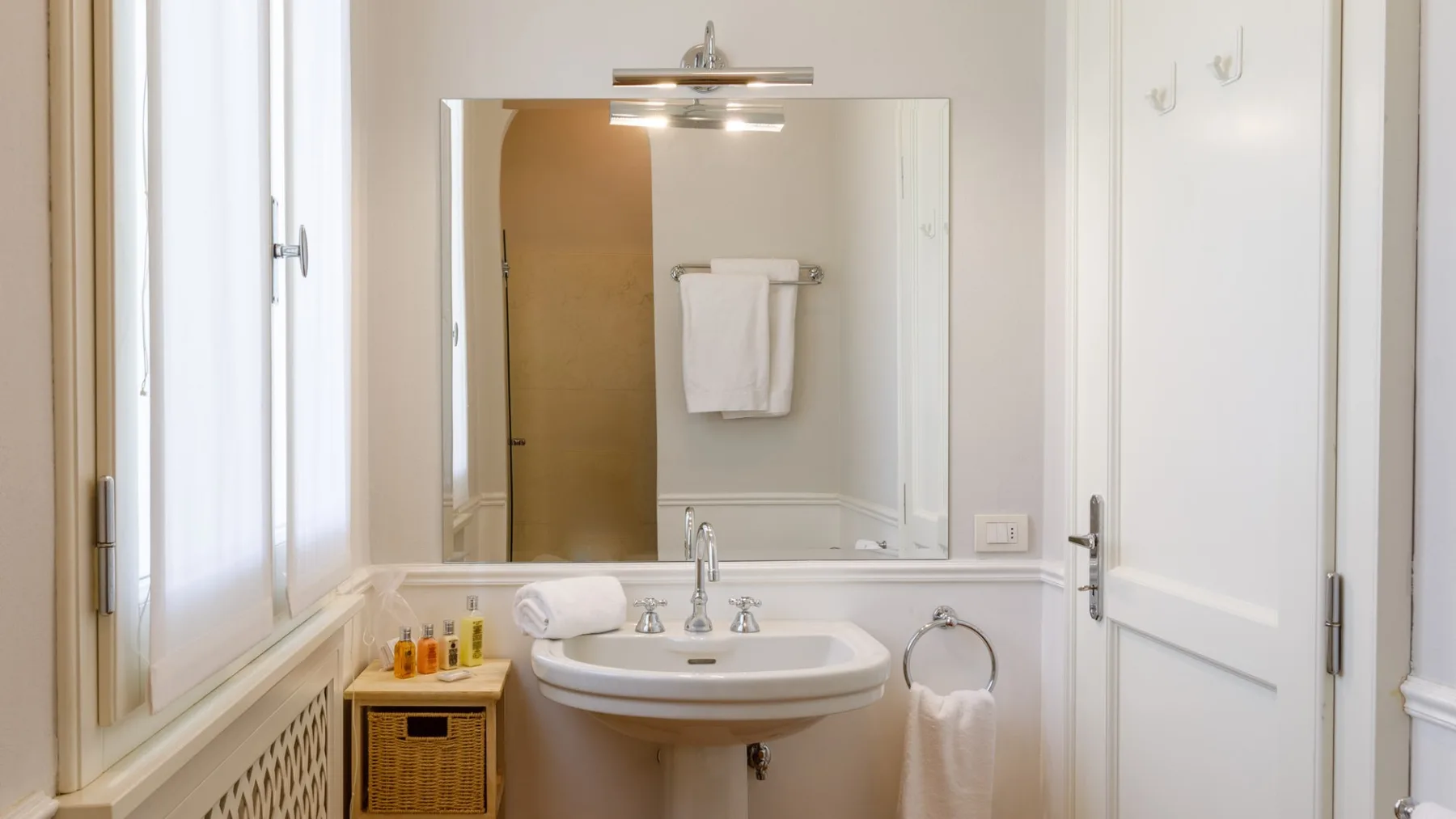 Un baño luminoso con lavabo de pedestal y un gran espejo de pared.