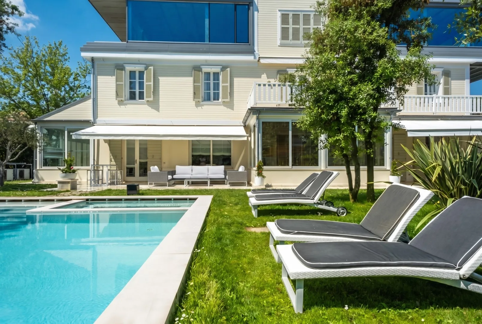 Una piscina y asientos de descanso están junto a una casa grande y un césped verde.