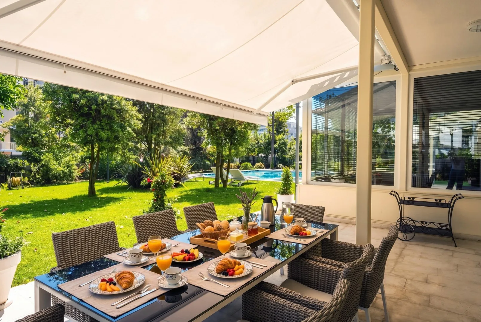 Un comedor exterior cubierto da a un jardín y una piscina.