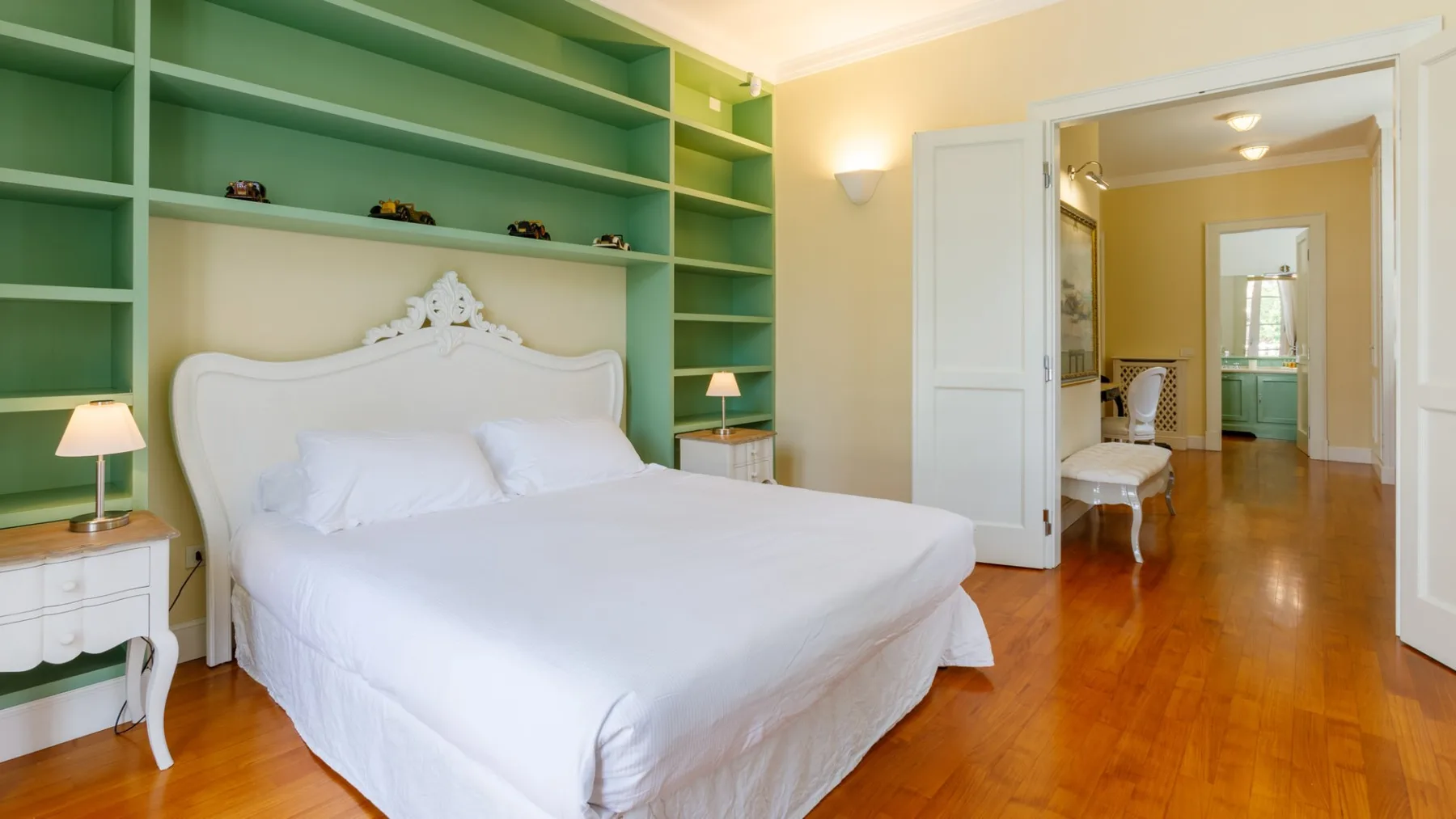 Un dormitorio con una cama blanca, estantes verdes empotrados y una puerta abierta.