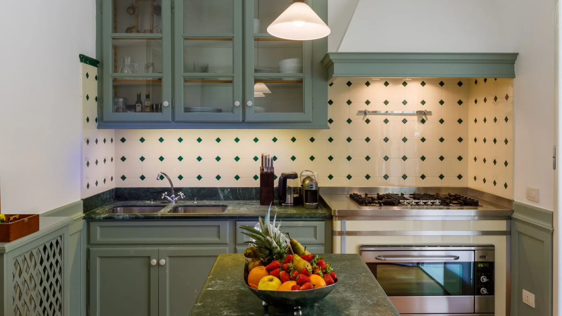 Una cocina con gabinetes verdes, un salpicadero de azulejos y un frutero sobre la encimera.