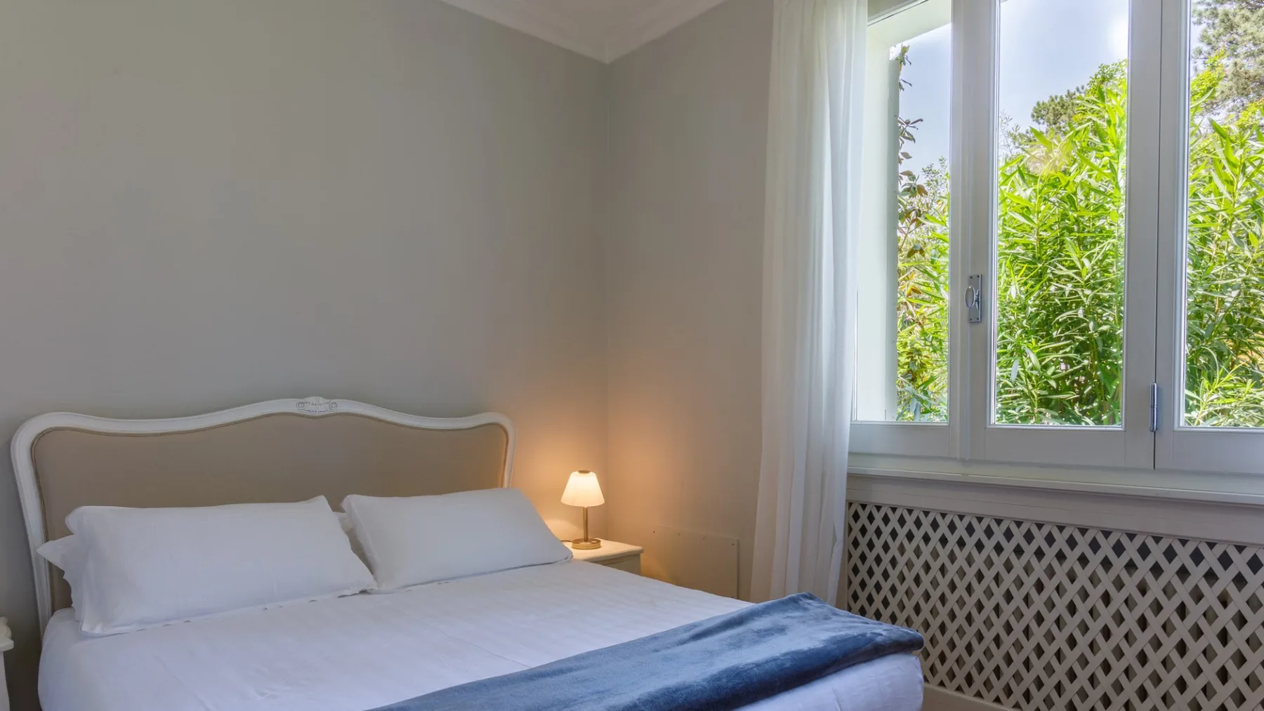 Un dormitorio con una cama bien tendida junto a una ventana luminosa.