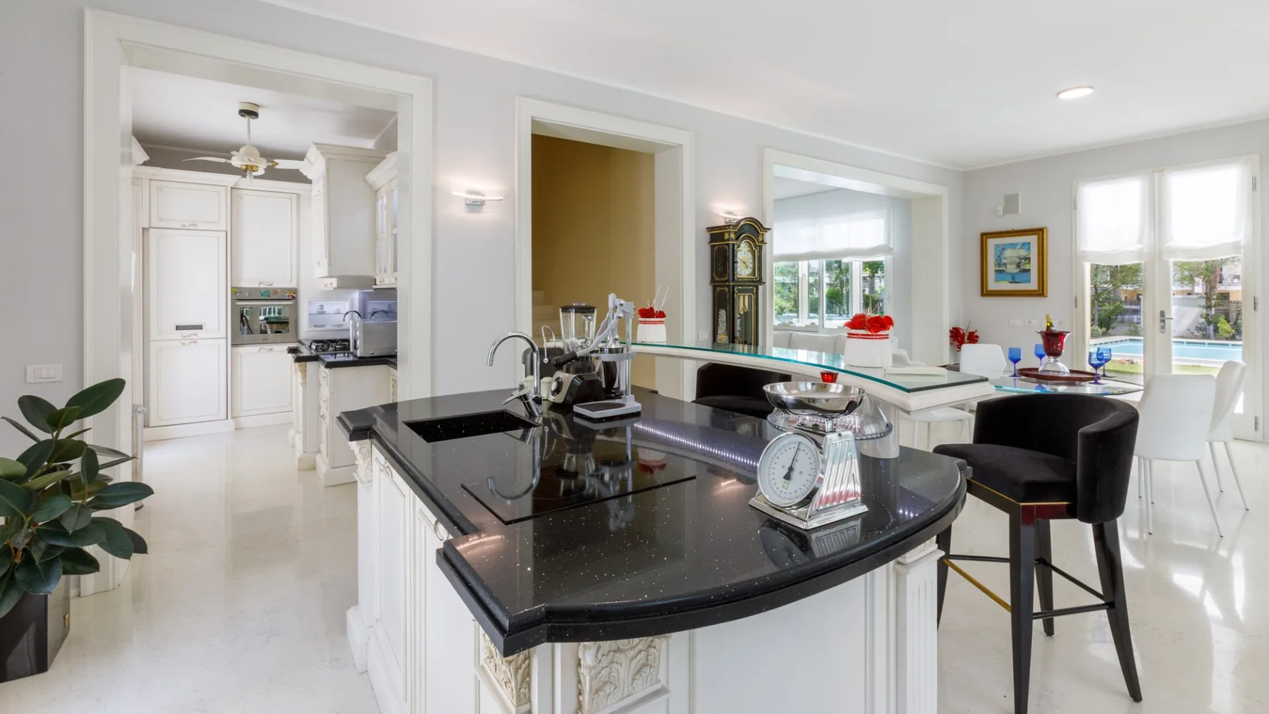 Una cocina luminosa con una isla negra y asientos de comedor junto a grandes ventanas.