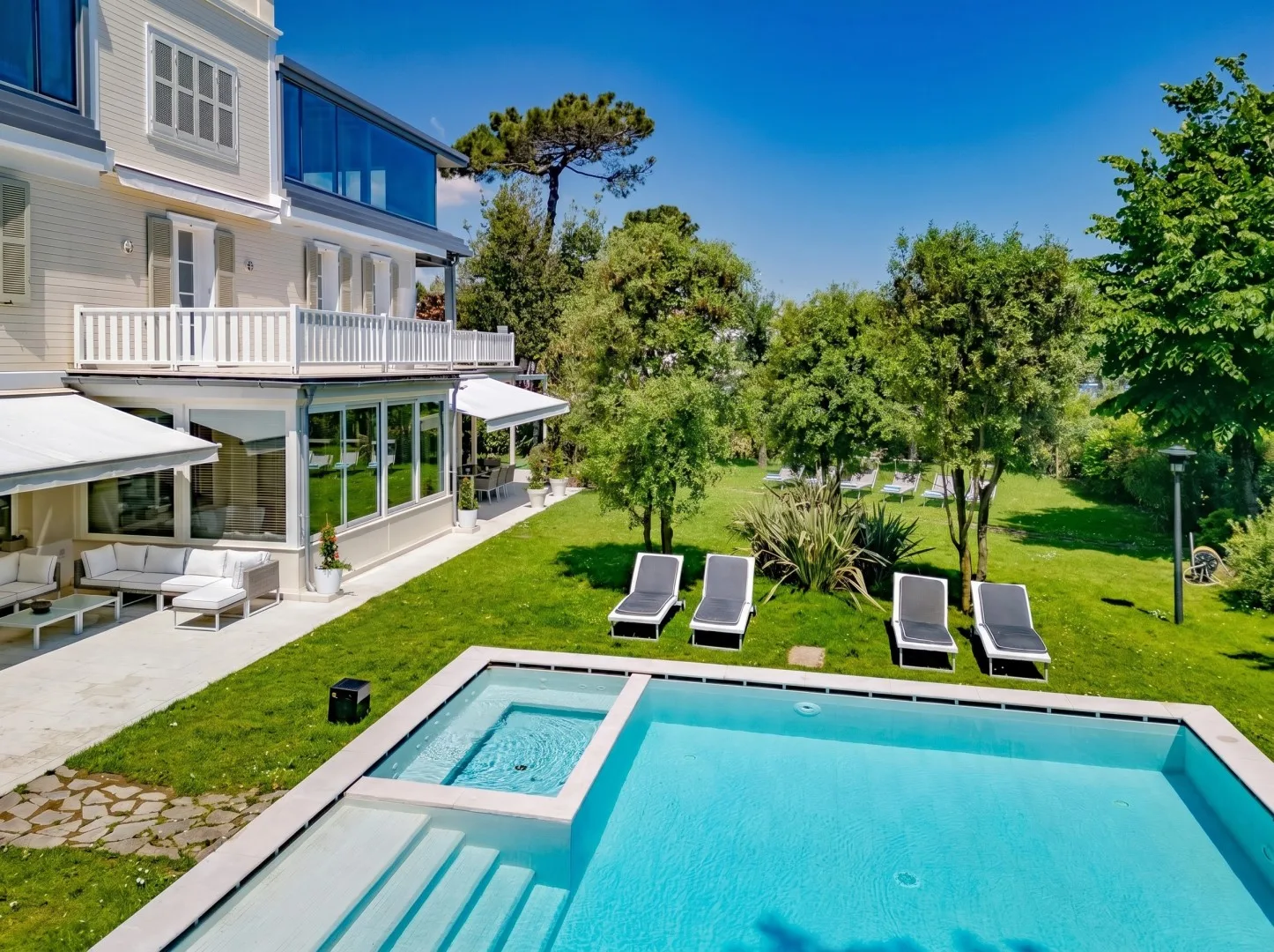 Un jardín con piscina, asientos reclinables y una casa grande.