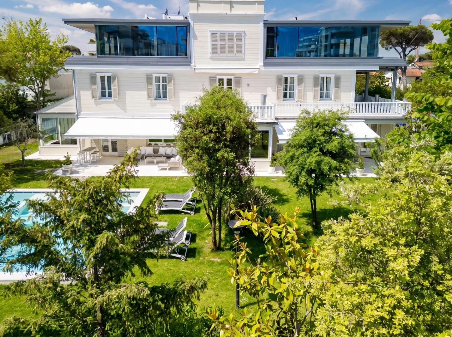 Una gran casa blanca da a un jardín paisajístico y una piscina al aire libre.