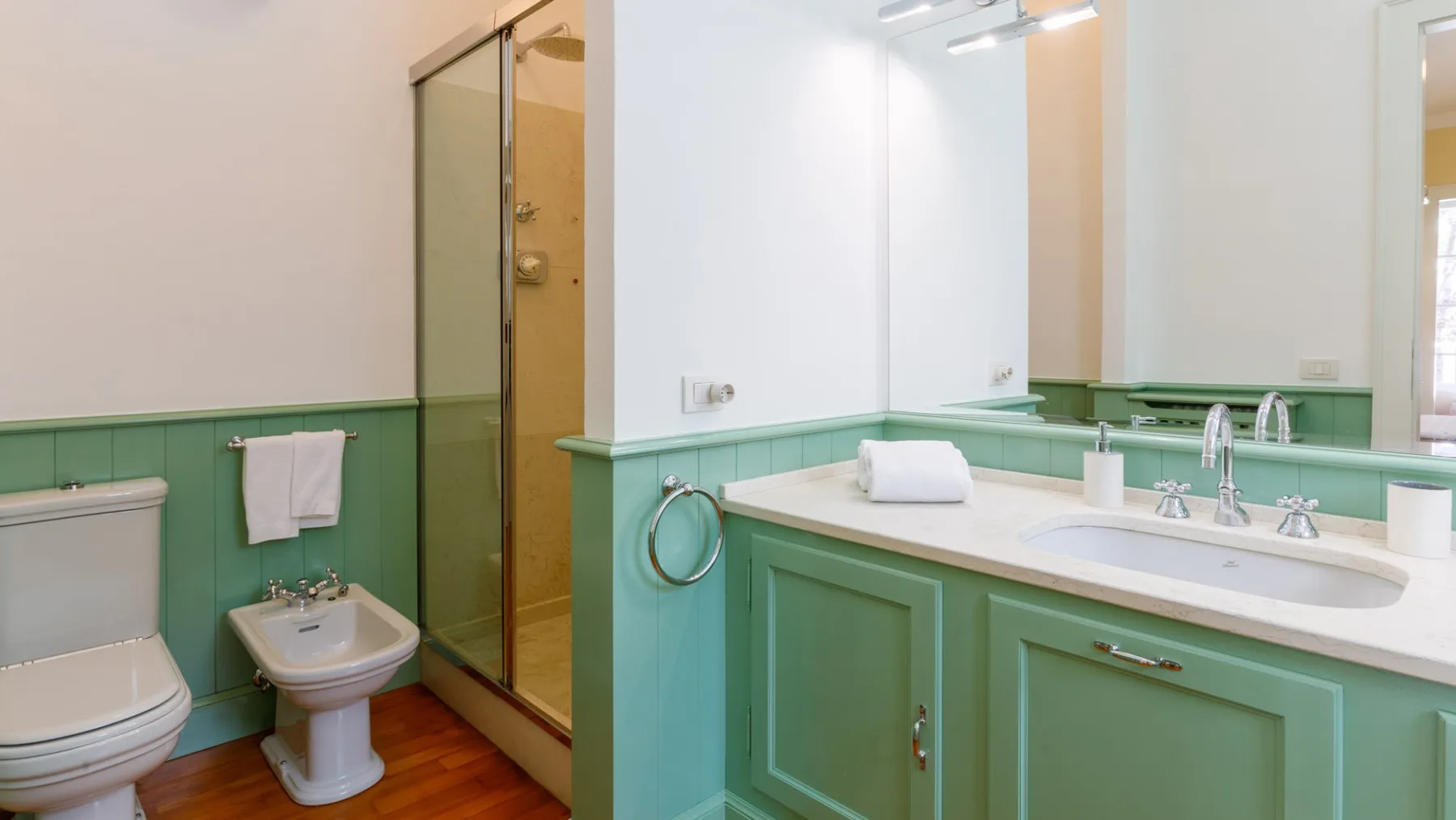 Un baño con tocador verde, lavabo y ducha con mampara de vidrio.