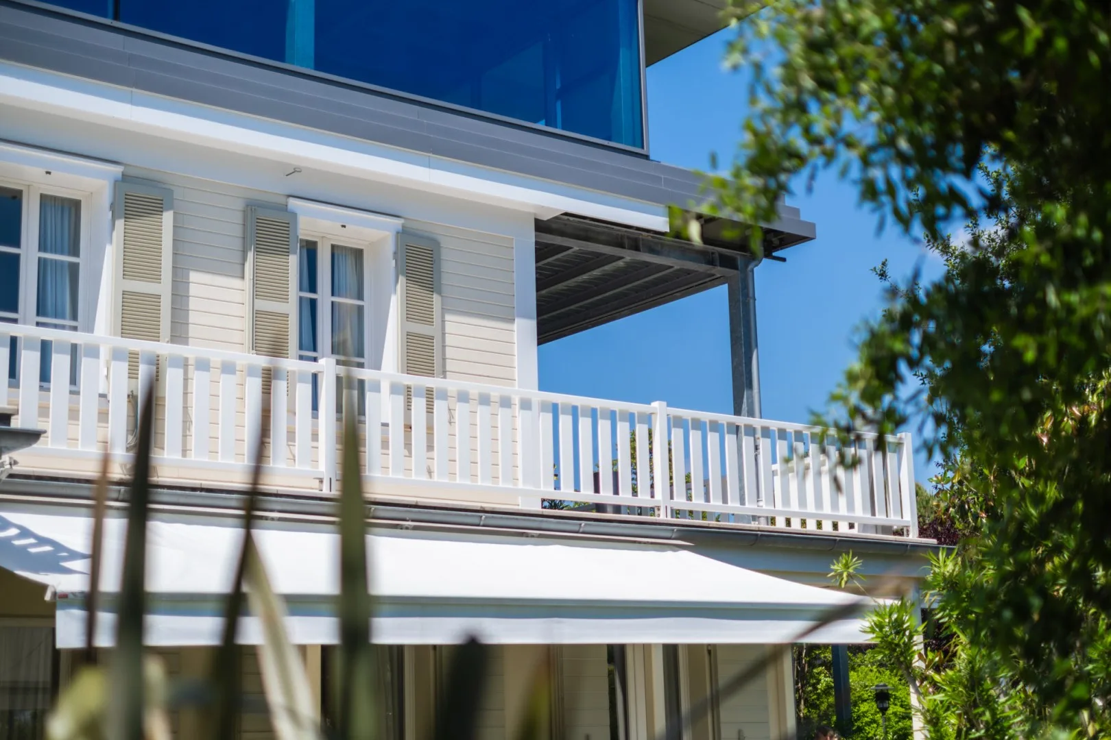 Una casa blanca tiene un balcón largo con barandilla blanca y ventanas a la sombra.