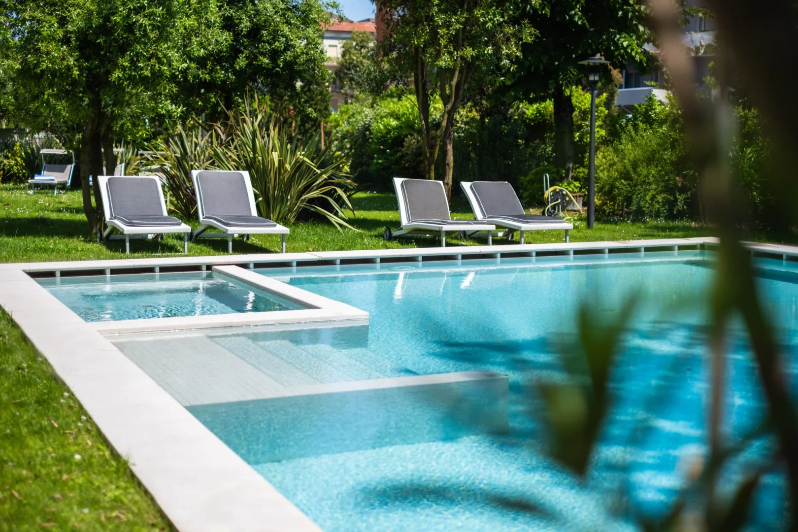 Una piscina al aire libre está rodeada de vegetación y asientos de descanso.