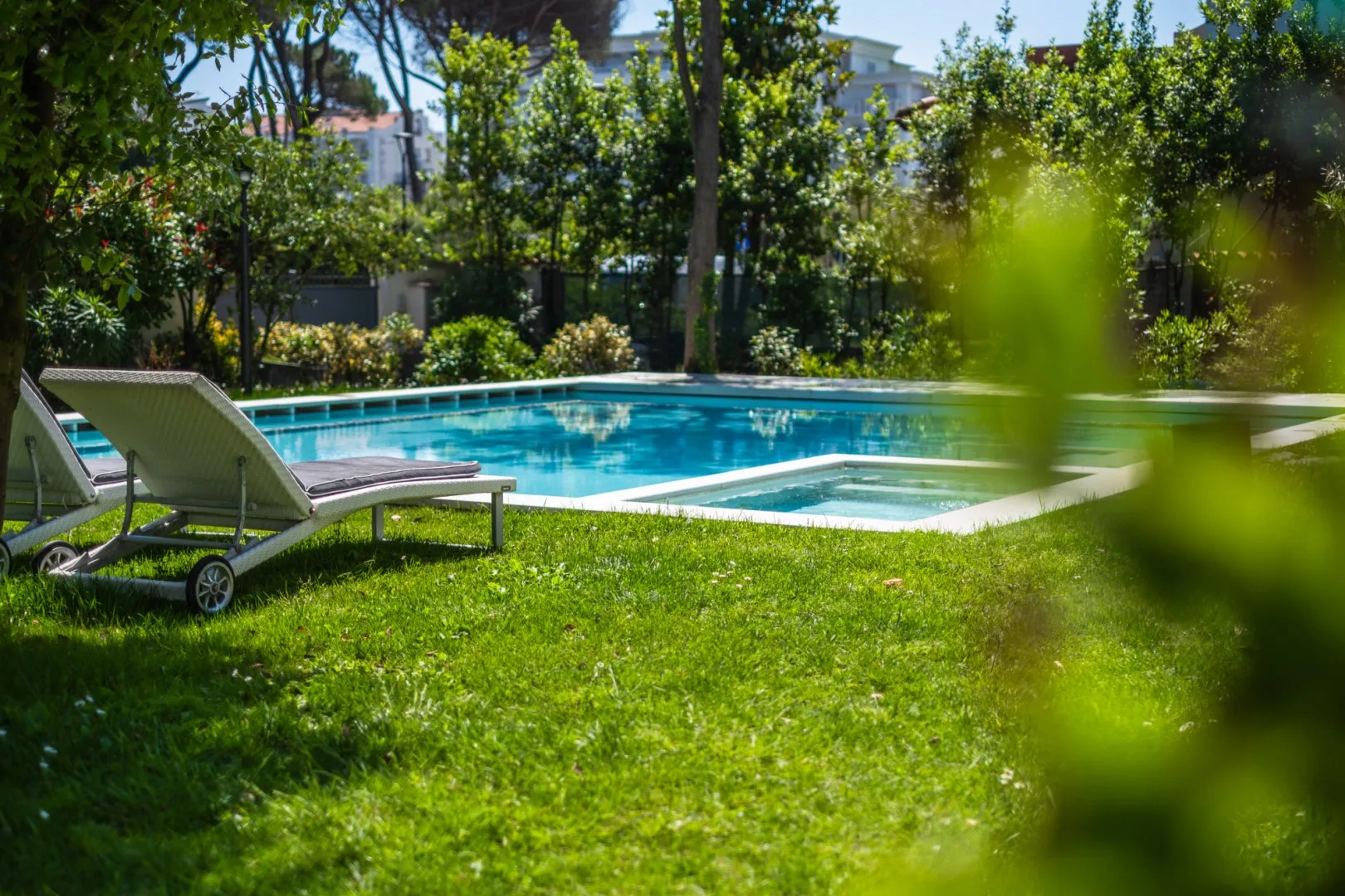 Una piscina al aire libre está junto a un césped y tumbonas reclinables.