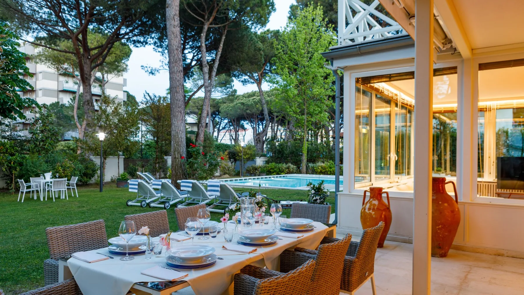 Una zona de comedor en el jardín, con la mesa puesta junto a una piscina y puertas de vidrio.