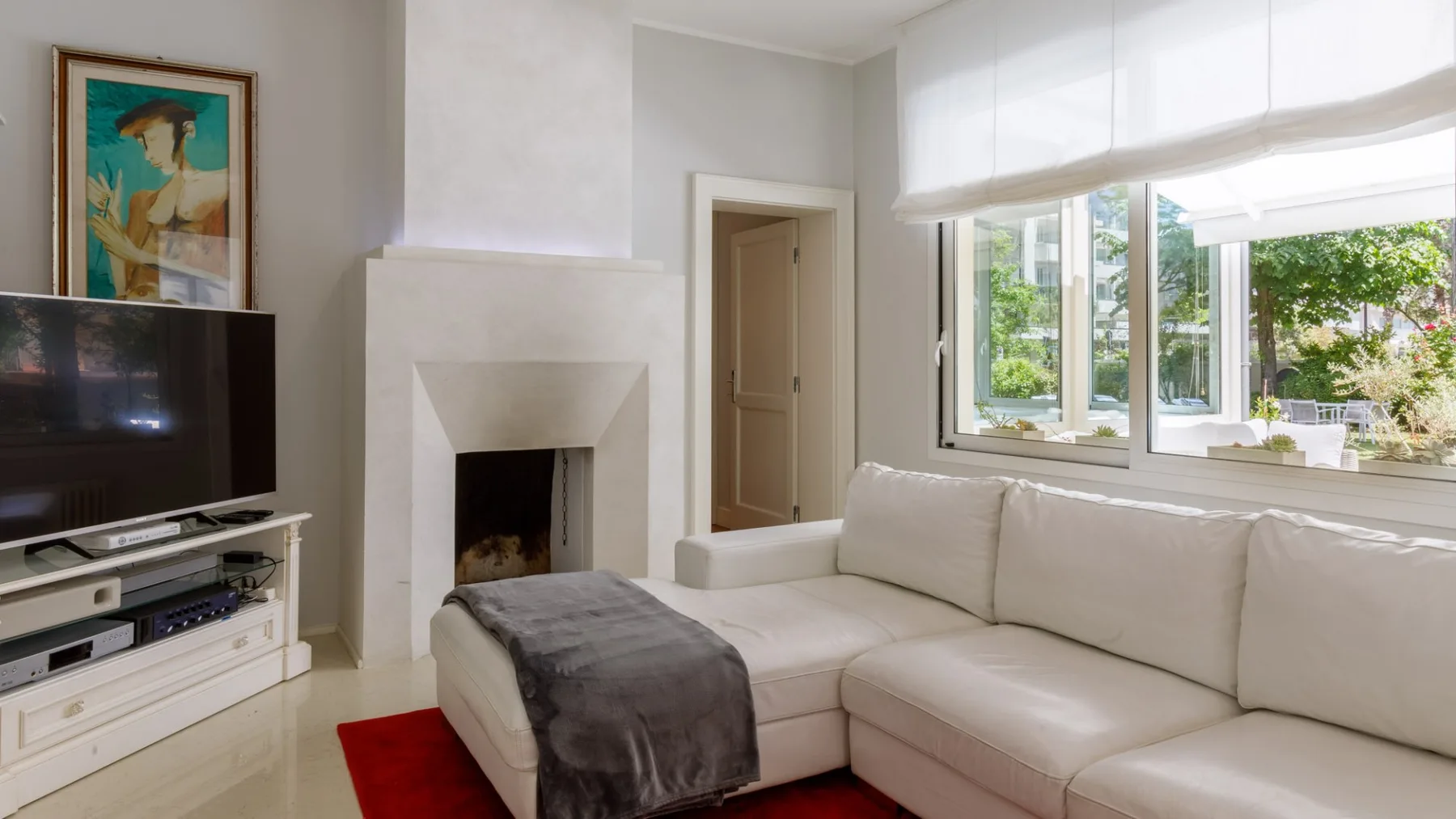 Una sala luminosa con un sofá seccional blanco y grandes ventanas.