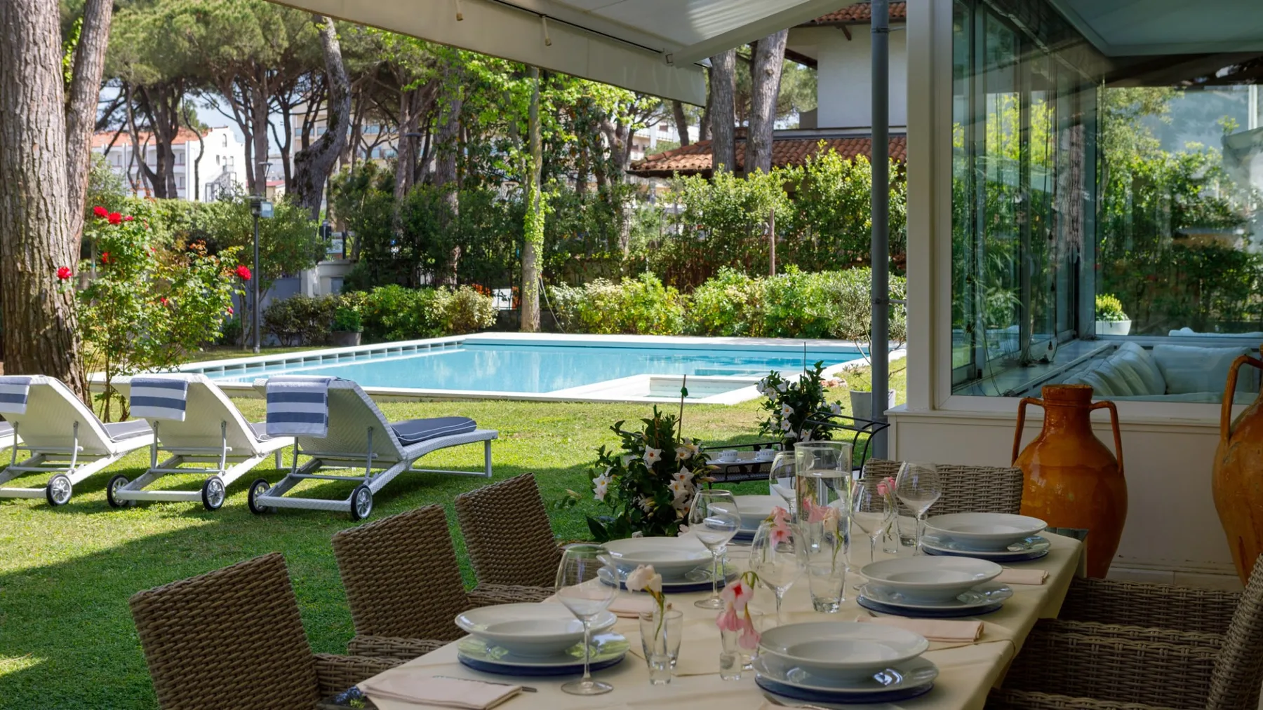 Una zona de comedor al aire libre cubierta da a una piscina y un jardín.