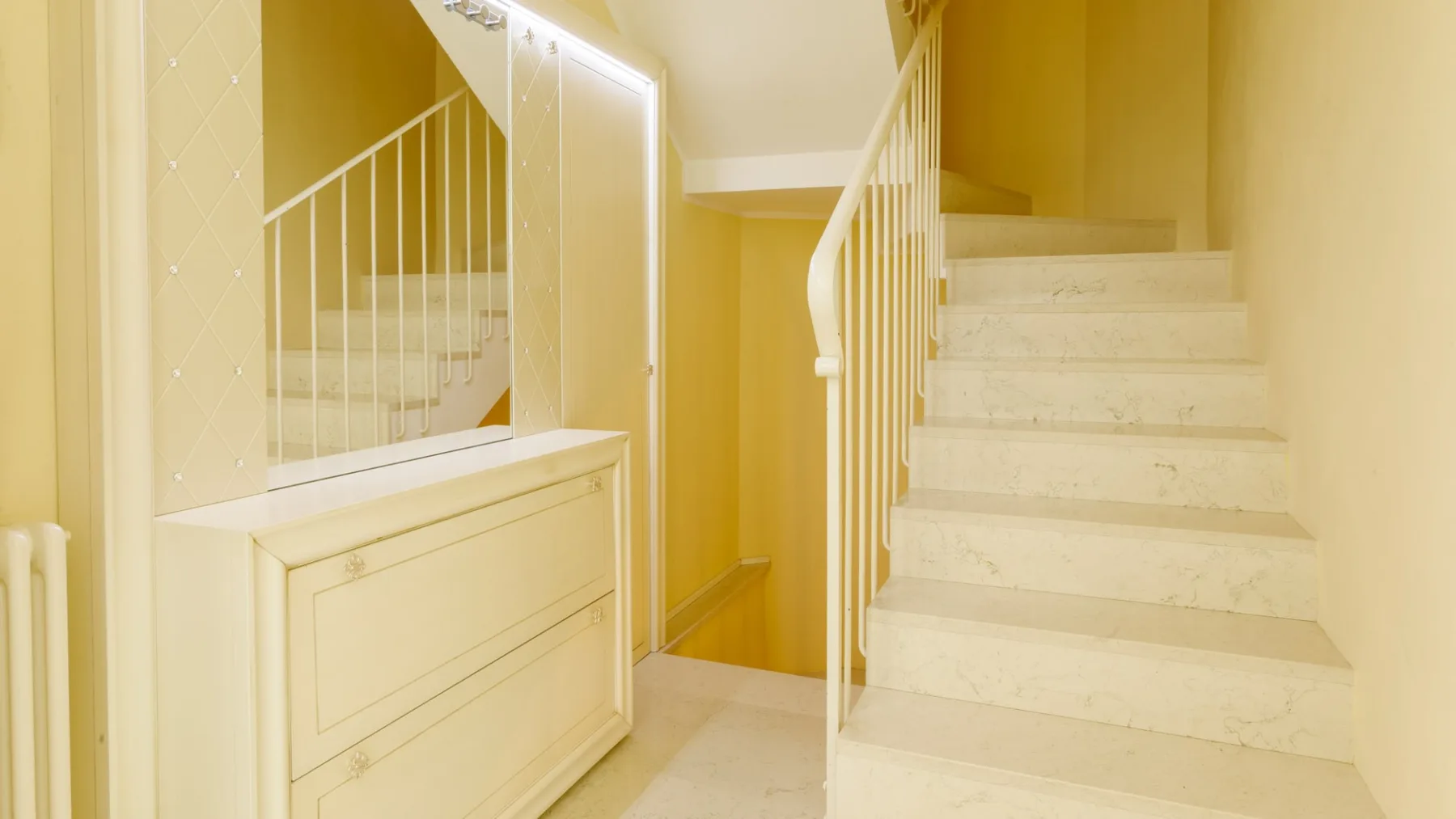 Una escalera interior con peldaños claros y una barandilla blanca.