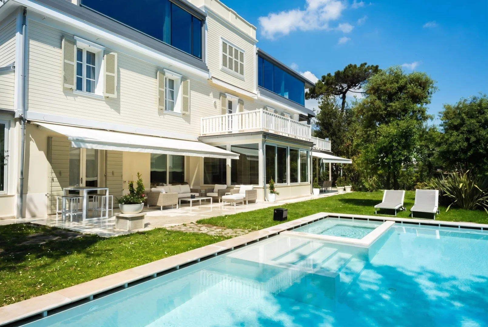 Una gran casa blanca da a una piscina y un patio amueblado.