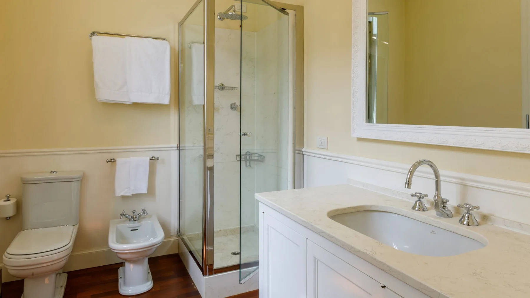 Un baño con ducha de vidrio, inodoro y lavabo bajo un espejo grande.