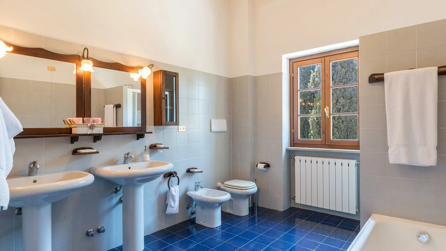 Un baño alicatado con lavabos, un inodoro y una ventana sobre un radiador.