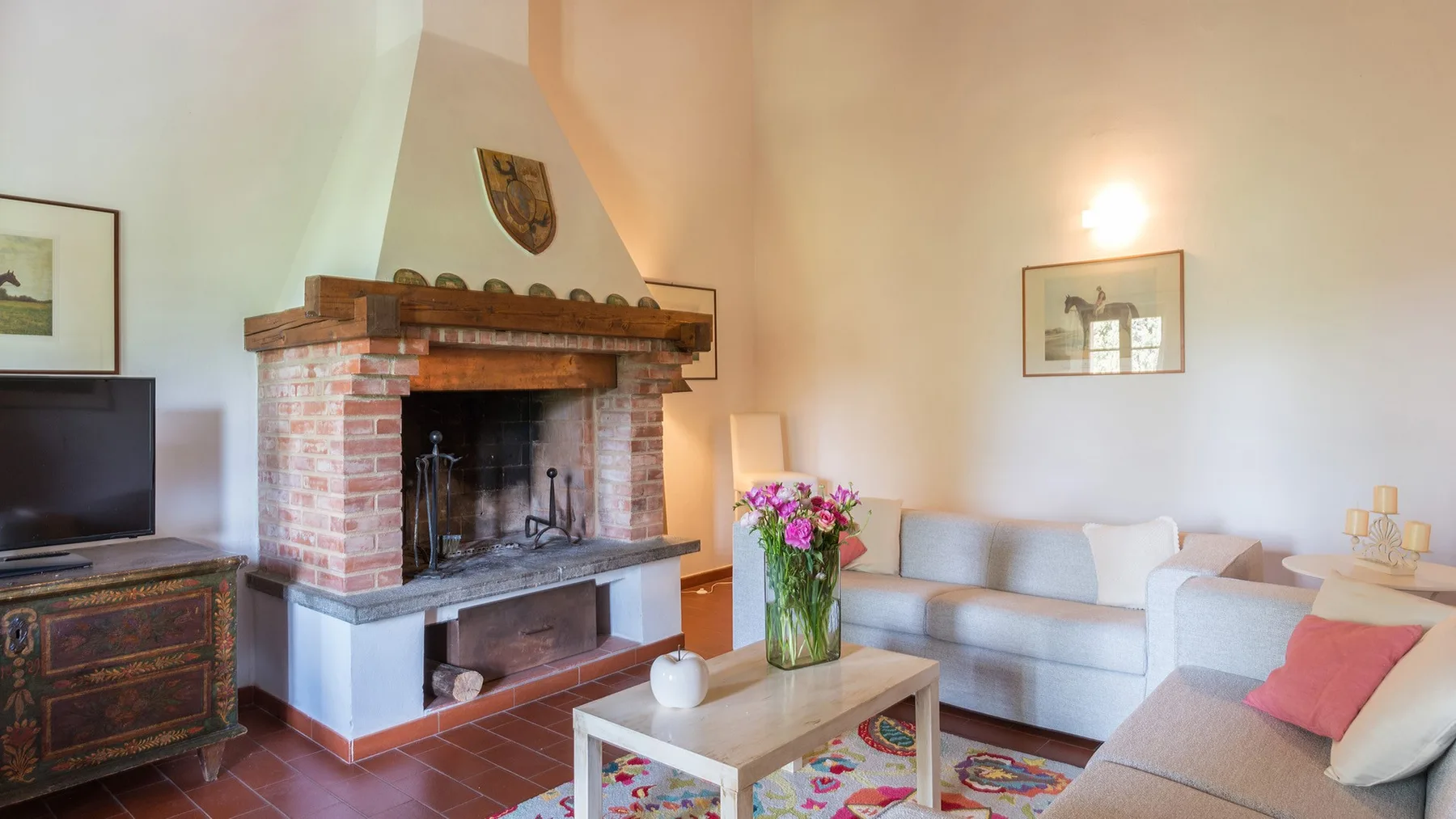 Una sala de estar con chimenea de ladrillo, asientos claros y flores sobre una mesa.