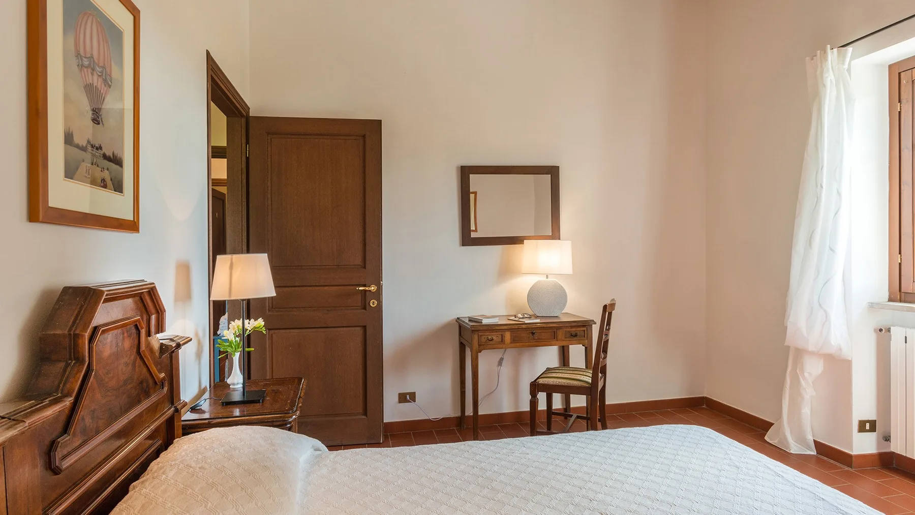 Un dormitorio con cama de madera, escritorio y una ventana con cortinas claras.