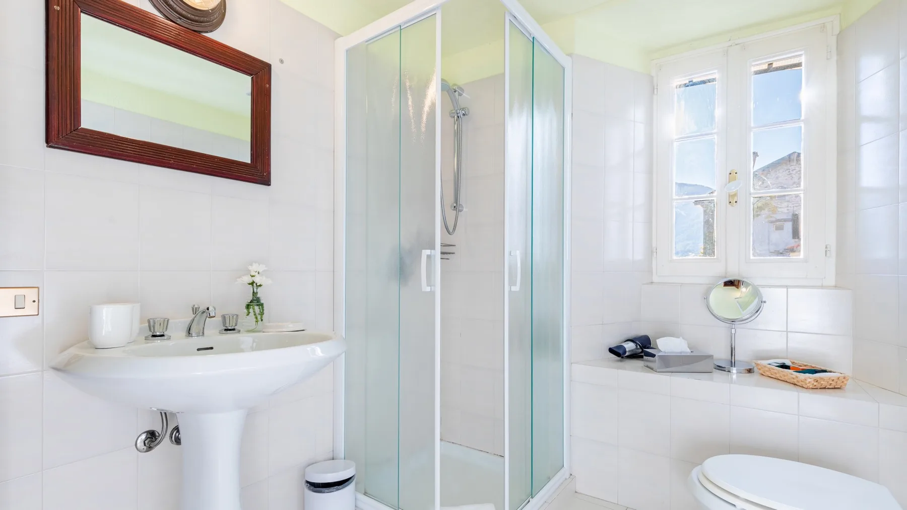 A bright tiled bathroom with a glass shower, sink, and toilet.