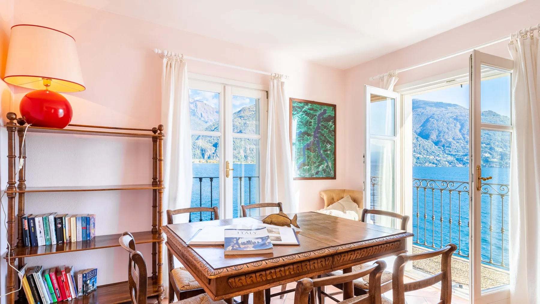 A dining area with a wooden table beside open doors overlooking the water.