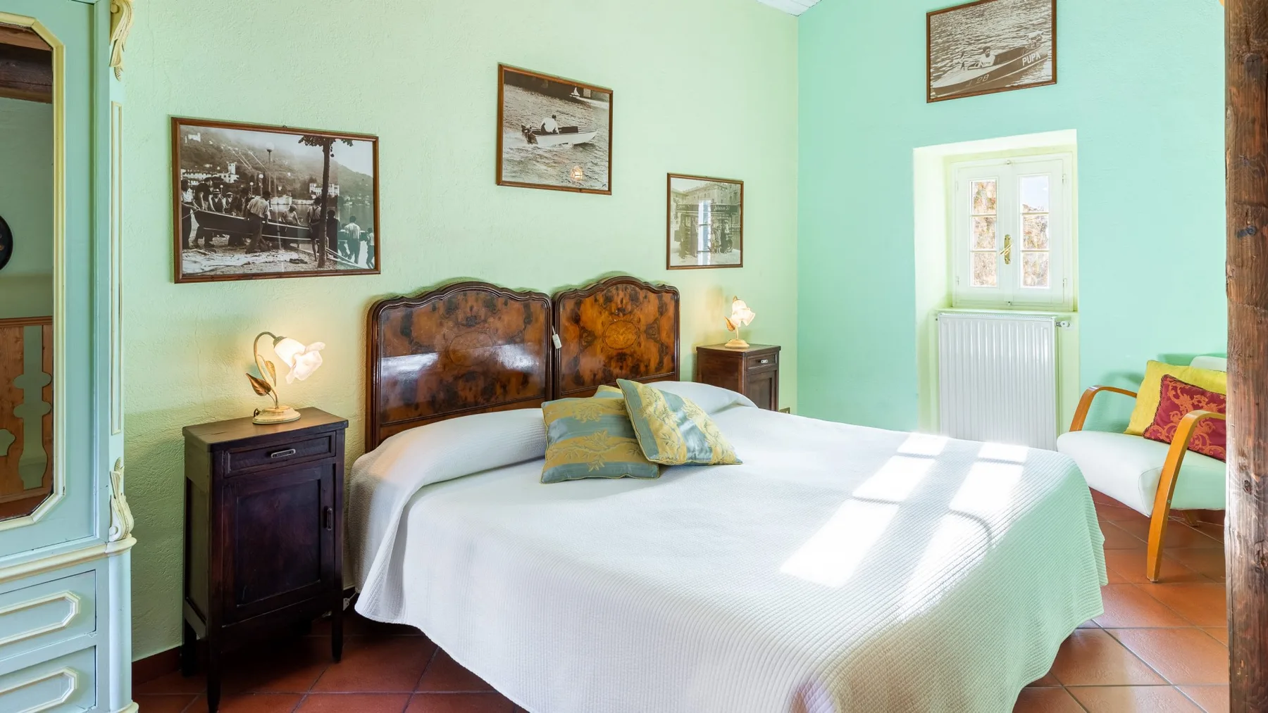 A bedroom with a neatly made bed, bedside tables, and framed pictures on mint-green walls.
