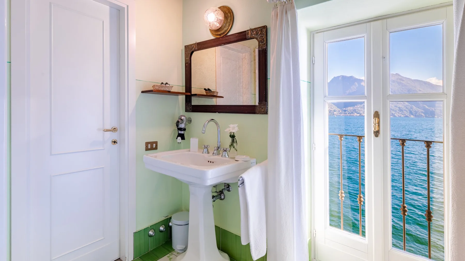 A bathroom with a pedestal sink and glass doors overlooking the water.
