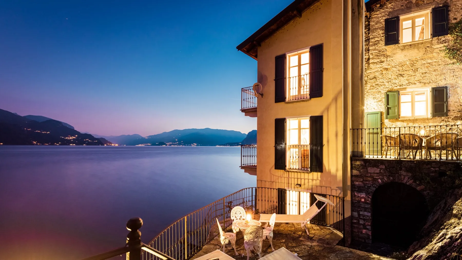 A lakeside building glows at dusk beside a terrace overlooking the water.