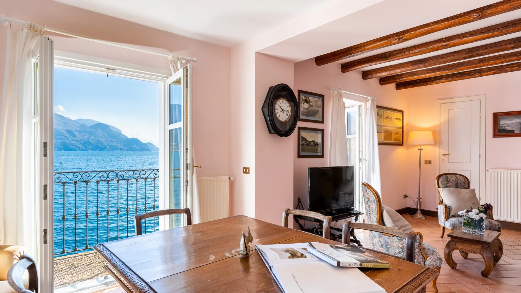 A bright living room opens onto a balcony overlooking the water and mountains.