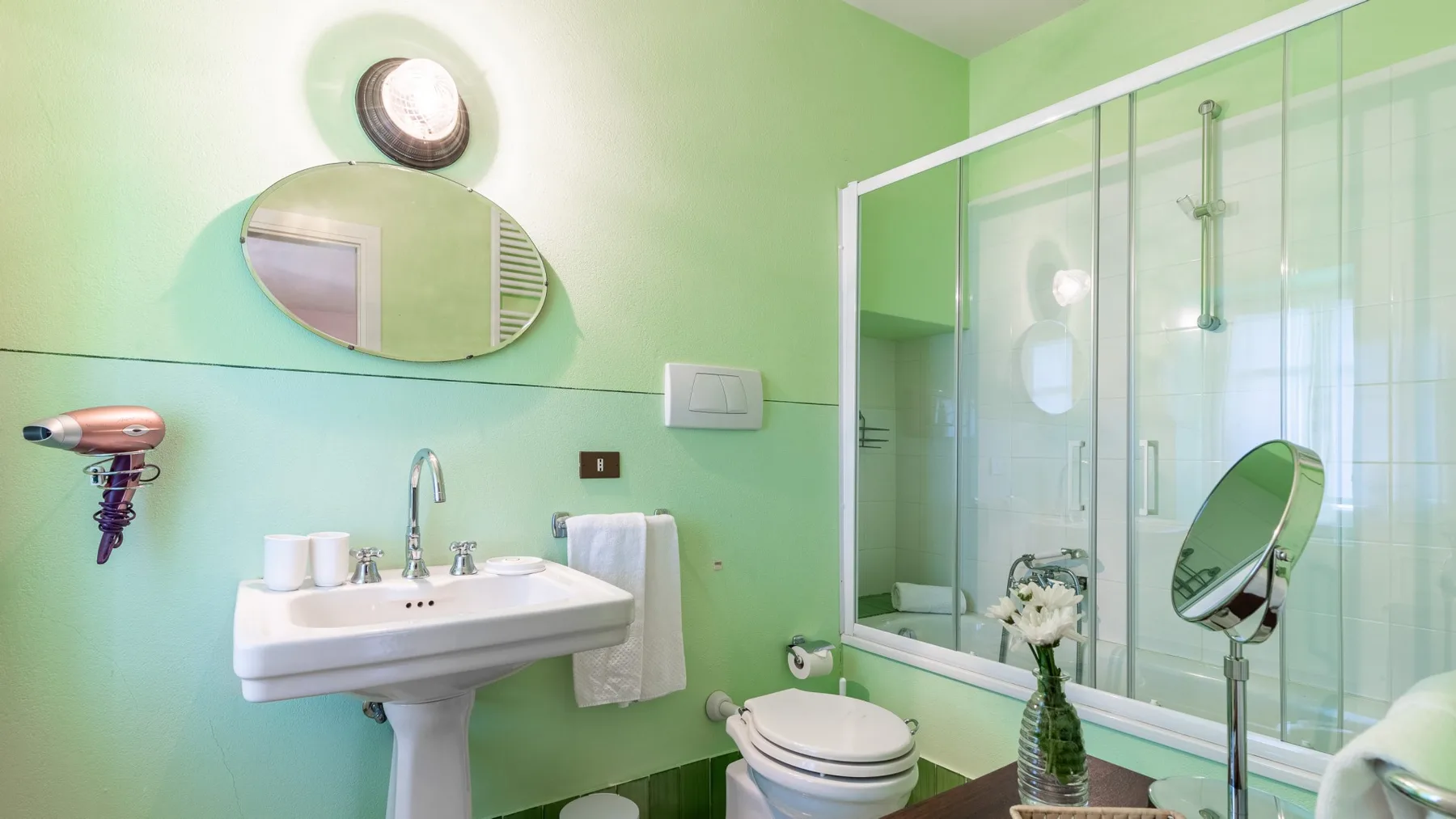 A mint-green bathroom with a sink, toilet, and glass shower enclosure.