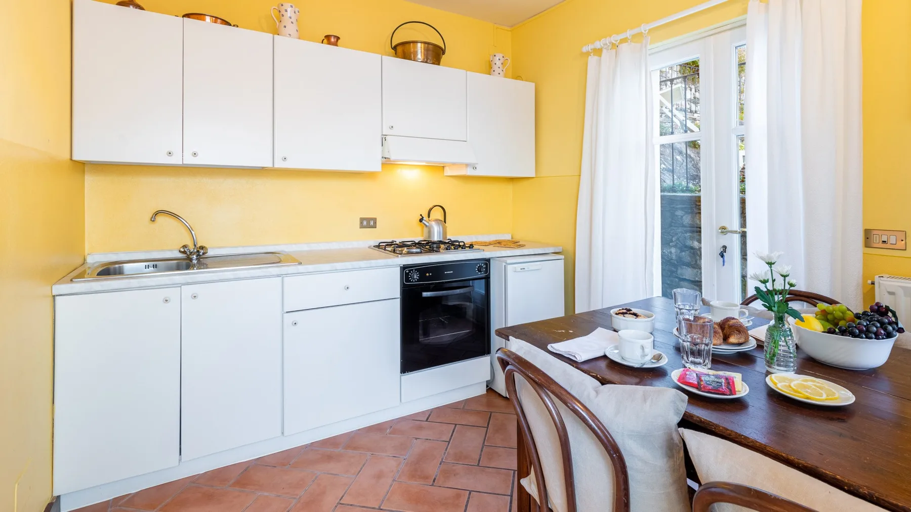 A bright yellow kitchen with white cabinets, a stove, and a dining table.