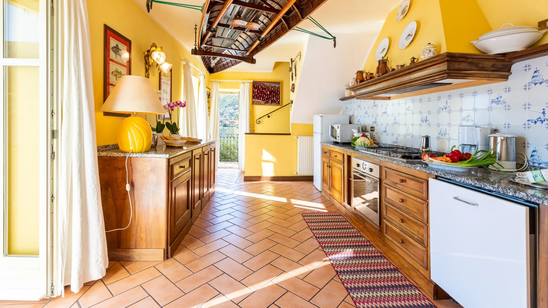 A bright kitchen with wooden cabinets, tiled flooring, and a long countertop.