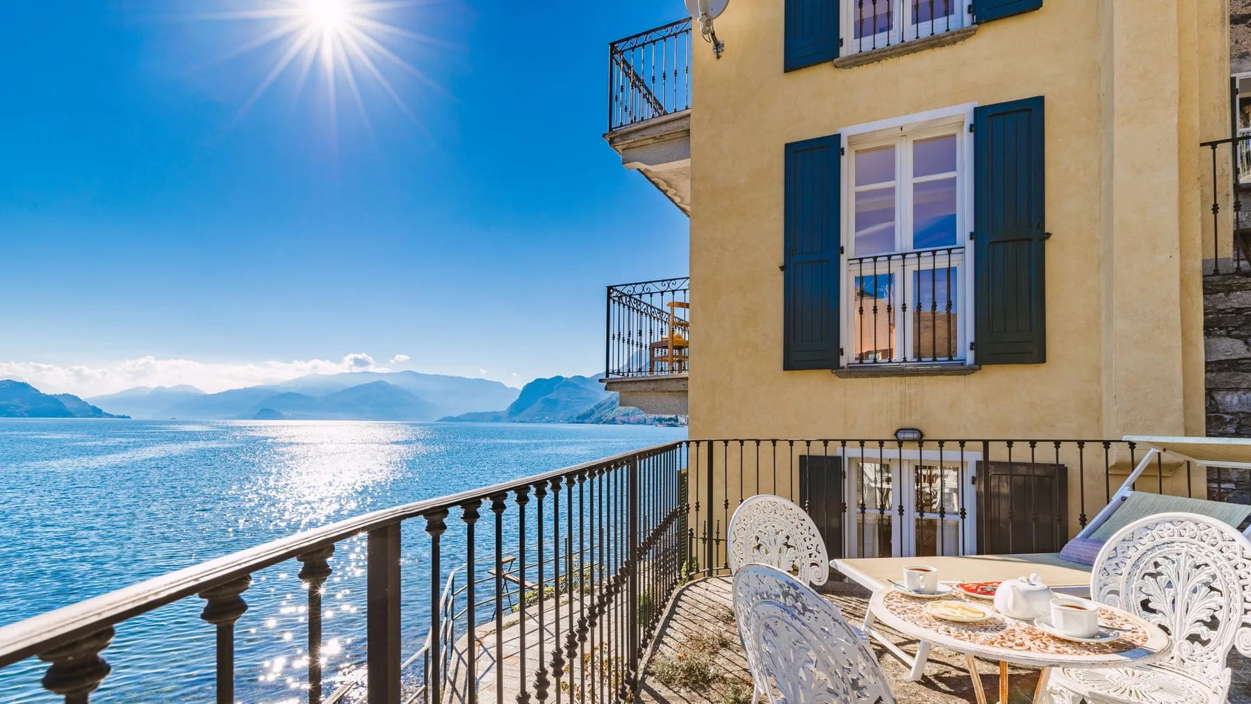 A waterside terrace with outdoor seating overlooks the lake and distant mountains.