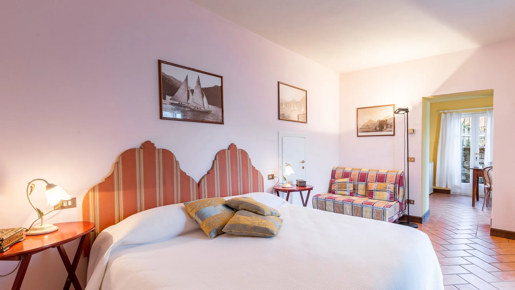 A bedroom with a large bed and a colorful settee beside the doorway.