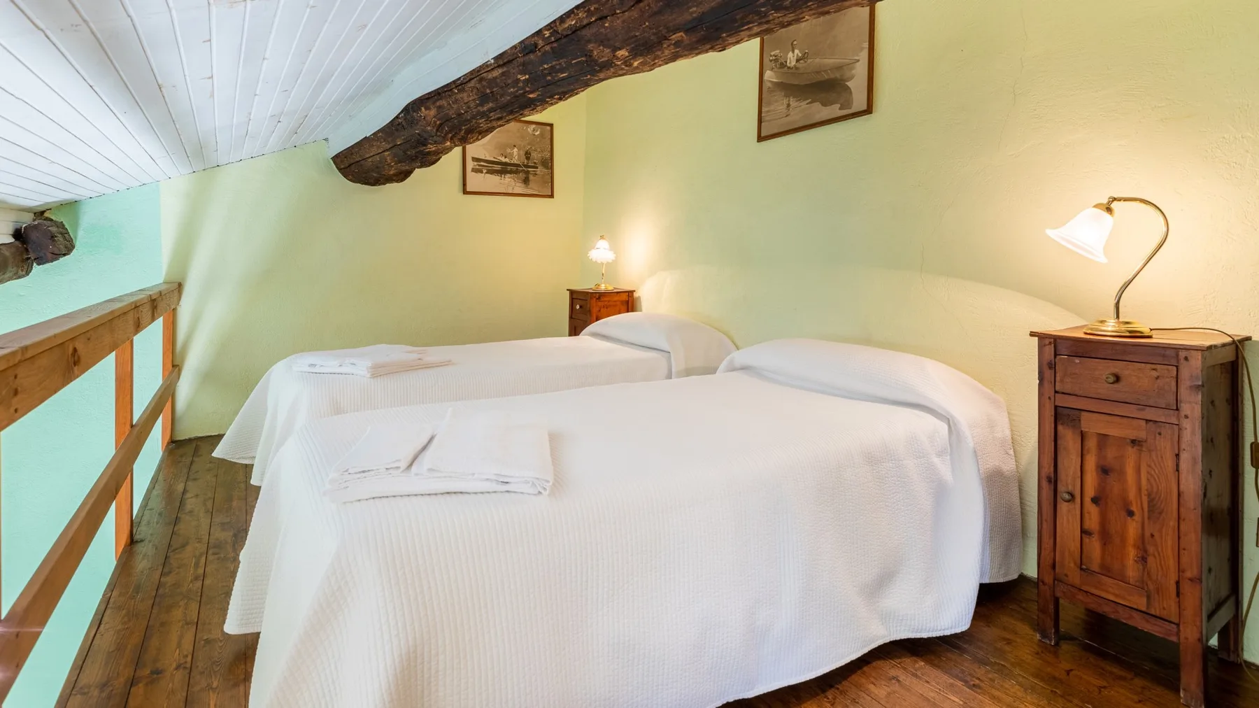 A bedroom with white-covered beds, wooden furniture, and an exposed ceiling beam.
