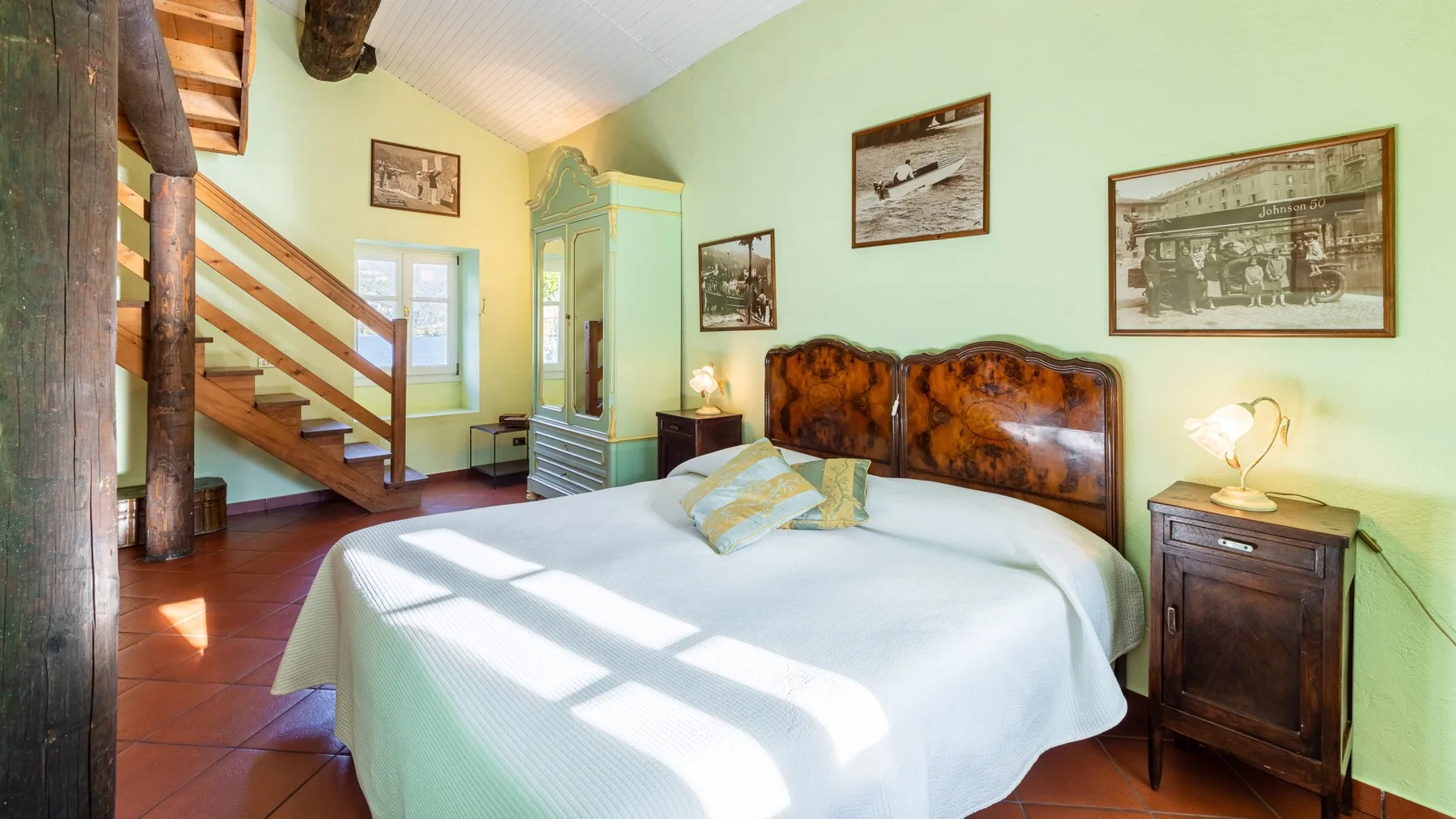 A bedroom with a neatly made bed and a wooden staircase.