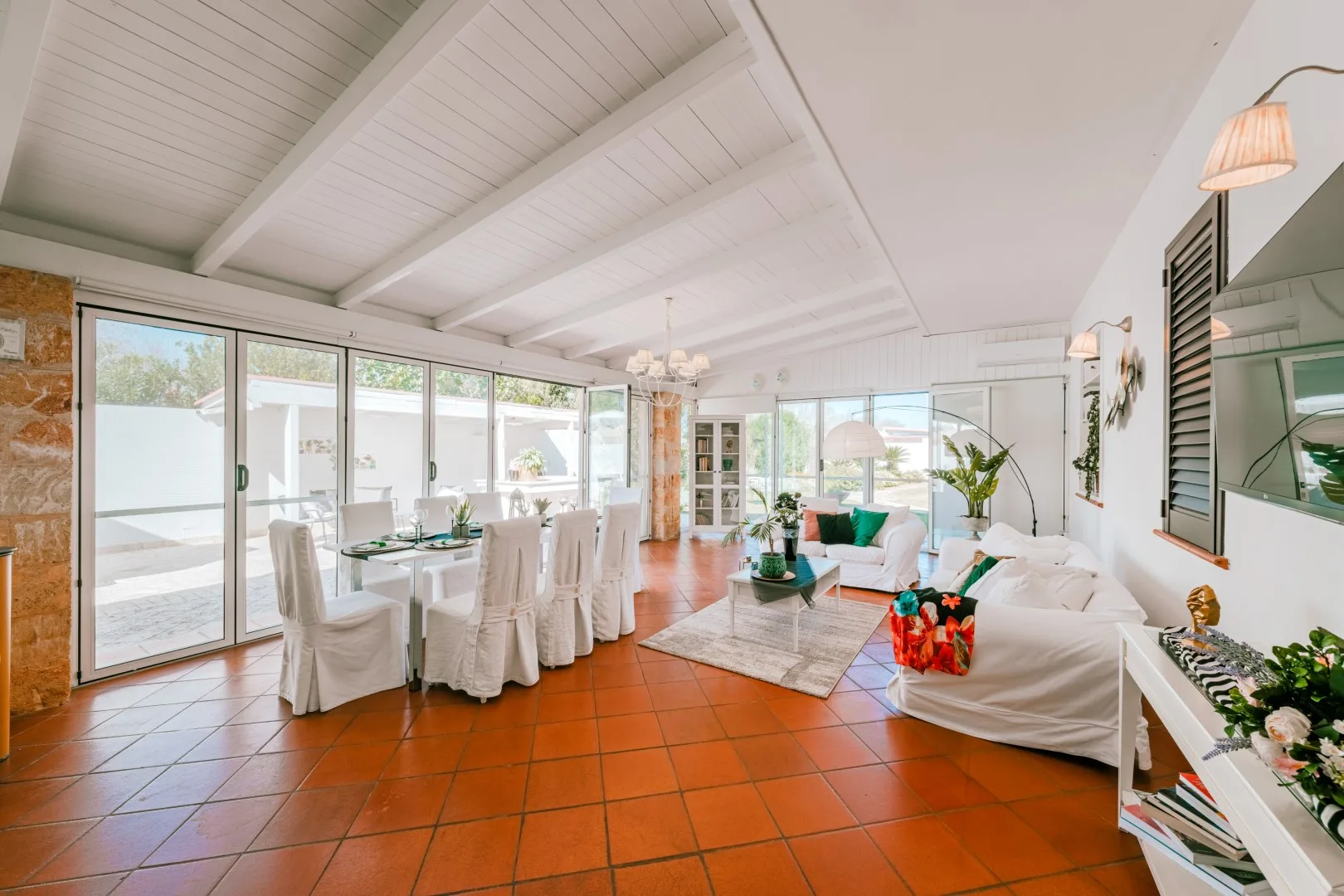 Bright open-plan living and dining area with a long table beside sliding glass doors.